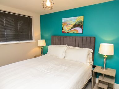 A bedroom with a double bed and white bedding two bedside tables with lamps and a teal accent wall with a painting at Apt 3 @ Hunter's Quay in Bridlington