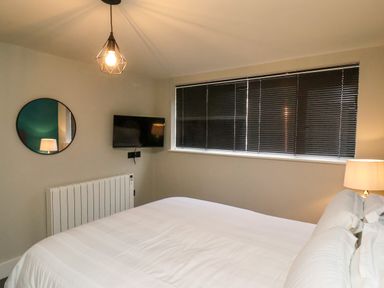 A bedroom with a bed a wall-mounted TV a round mirror and a window with blinds at Apt 3 @ Hunter's Quay in Bridlington