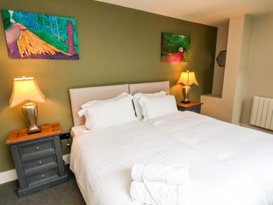 A bedroom with a double bed two bedside tables with lamps and paintings on an olive green wall at Apt 3 @ Hunter's Quay in Bridlington