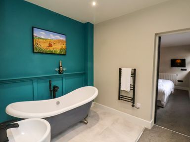 A bathroom with a clawfoot tub a towel rack and a painting on a teal wall at Apt 3 @ Hunter's Quay in Bridlington