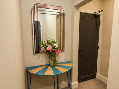 A hallway with a decorative half-moon table holding a vase of flowers and a geometric wall mirror at Apt 3  Hunter's Quay in Bridlington