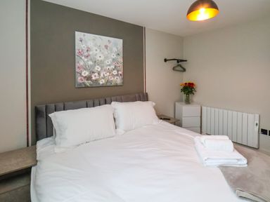 A bedroom with a large bed white pillows folded white towels a floral painting and a vase of flowers at Apt 6 @ Hunter's Quay in Bridlington