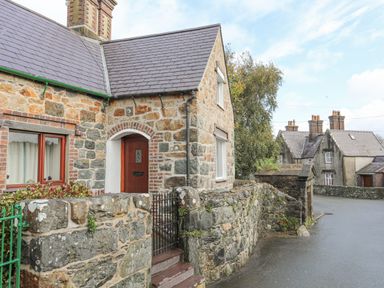 A stone house with a wooden door and fenced garden next to a stone wall along a street at 5 The Crescent in Caernarfon