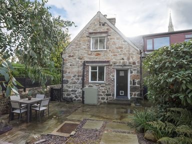 A stone house with two windows and a black door in a garden with a table and four chairs at 5 The Crescent in Caernarfon