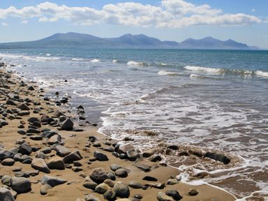 A sandy beach with scattered rocks and waves coming ashore with a mountain range in the background at 5 The Crescent in Caernarfon