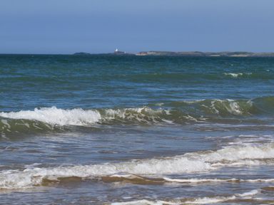 A view of ocean waves with a distant island and lighthouse at 5 The Crescent in Caernarfon