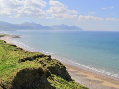 A coastal landscape with grassy cliffs a sandy beach and mountains in the distance at 5 The Crescent in Caernarfon