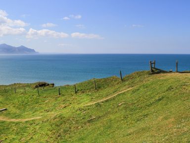 A coastal grassy hillside with a wooden fence and ocean view at 5 The Crescent in Caernarfon