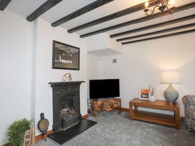 A living room with a fireplace television on a wooden stand table with a lamp and artwork at 5 The Crescent in Caernarfon