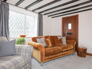 A living room with a brown sofa and a plaid armchair near a wooden door and window at 5 The Crescent in Caernarfon
