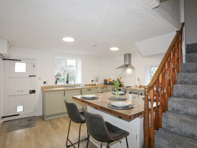 A kitchen with an island set for four, a staircase with wooden banister, a door, and a window at 5 The Crescent in Caernarfon