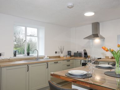 A kitchen with cabinets a window a sink an oven a stove and a dining table with plates and glasses at 5 The Crescent in Caernarfon