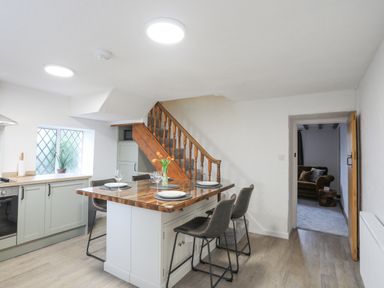 A kitchen with a wooden island and bar stools near a staircase and an open door to a living room at 5 The Crescent in Caernarfon