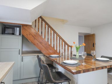 A kitchen dining area with a wooden table topped with plates glasses and a vase of flowers and a staircase at 5 The Crescent in Caernarfon