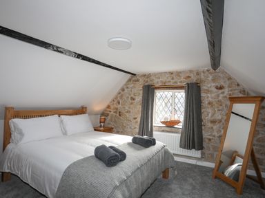 A bedroom with a wooden bed frame white bedding folded towels stone wall window with curtains and a standing mirror at 5 The Crescent in Caernarfon