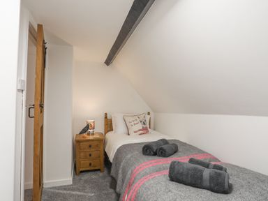 A bedroom with a single bed a wooden bedside table with a lamp and an open wooden door at 5 The Crescent in Caernarfon