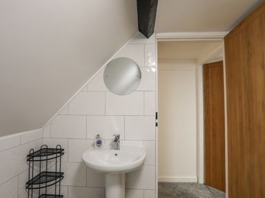 A bathroom with a pedestal sink mirror and black corner shelving unit at 5 The Crescent in Caernarfon
