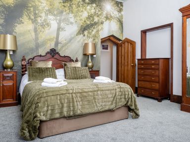 A bedroom with a bed covered in green bedding two bedside tables with lamps a small door and a wooden dresser at Watermouth Castle West Tower Apartment Berrynarbor near Ilfracombe