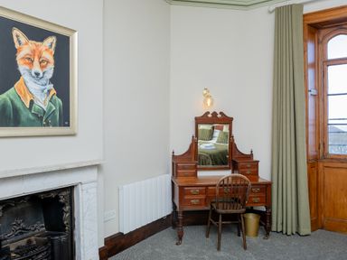 A room with a wooden vanity table and chair next to a window and a fireplace with a fox painting on the wall at Watermouth Castle West Tower Apartment Berrynarbor near Ilfracombe