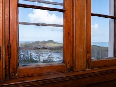View of boats on water and hills through a wooden-framed window at Watermouth Castle West Tower Apartment Berrynarbor near Ilfracombe