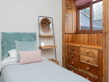 A bedroom with a single bed a round mirror on a stand and a wooden chest of drawers at Watermouth Castle West Tower Apartment Berrynarbor near Ilfracombe