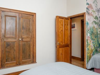 A bedroom with a wooden closet door a wooden open door a bed with a light blue quilt and a floral wallpaper at Watermouth Castle West Tower Apartment in Berrynarbor near Ilfracombe