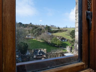 A rural landscape with green fields trees and houses viewed from a wooden window at Watermouth Castle West Tower Apartment Berrynarbor near Ilfracombe