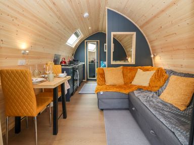 A pod interior with dining table and orange chairs opposite a grey sofa with orange and grey cushions at Heron Pod Nantmawr near Trefonen
