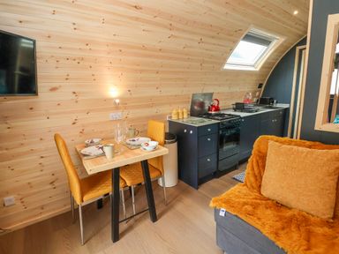 A small kitchen and dining area with a wooden table set for two and orange chairs at Heron Pod in Nantmawr near Trefonen