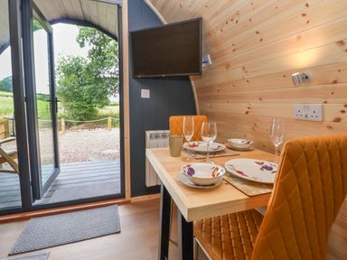 A dining area with a table set for two next to an open door showing an outdoor scene at Heron Pod in Nantmawr near Trefonen