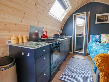 A kitchen with black cabinets and a red kettle next to a bed with floral bedding at Heron Pod in Nantmawr near Trefonen