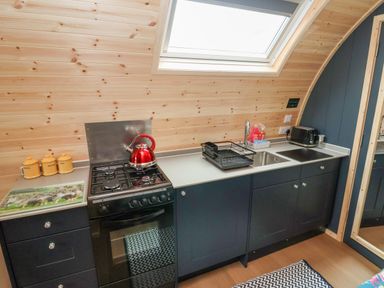 A kitchen with black cabinets a gas stove and oven a red kettle a sink a drying rack and a toaster at Heron Pod in Nantmawr near Trefonen