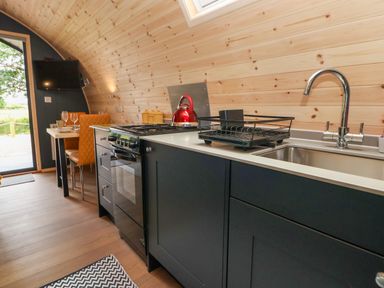 A kitchen with black cabinets a sink a stove a red kettle and a dining table with two chairs at Heron Pod Nantmawr near Trefonen