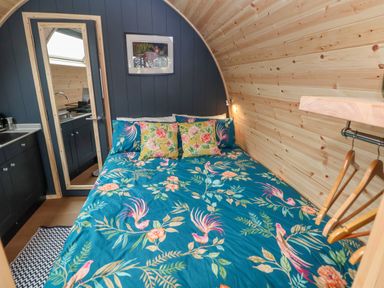A bedroom with a bed with floral bedding wooden walls a door with mirror and black cabinets at Heron Pod Nantmawr near Trefonen