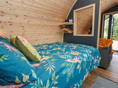 A bedroom with a floral blue bedspread a mirror wooden hangers and a sitting area with an orange blanket at Heron Pod Nantmawr near Trefonen