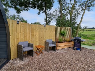 An outdoor seating area with two chairs a small table a planter wooden fence and a barbecue grill at Heron Pod Nantmawr near Trefonen