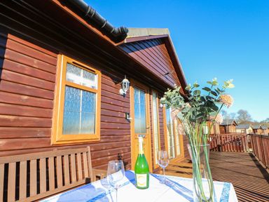 A wooden deck with a table set with a bottle and glasses outside a cabin at The Fairhaven in Tunstall near Catterick North Yorkshire