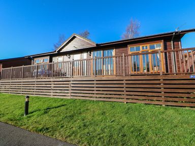 A wooden cabin with a fenced porch and green lawn at The Fairhaven in Tunstall near Catterick North Yorkshire