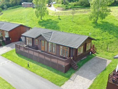 An aerial view of a wooden lodge with a fenced deck and a gravel driveway surrounded by grass at The Fairhaven in Tunstall near Catterick North Yorkshire