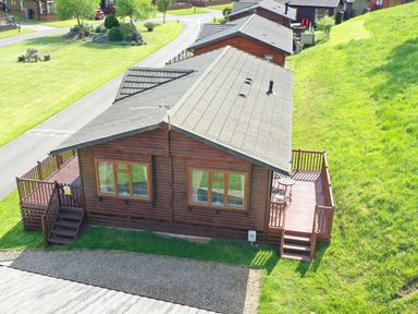 A wooden cabin with a deck and steps on both sides with grass and a road nearby at The Fairhaven in Tunstall near Catterick North Yorkshire
