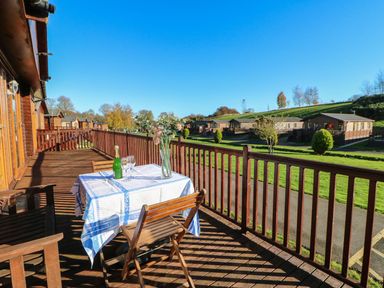A wooden balcony with a table covered with a tablecloth and chairs overlooking cabins and grassy area at The Fairhaven in Tunstall near Catterick North Yorkshire