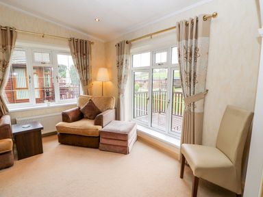 A living room with armchairs a floor lamp a side table and windows with curtains at The Fairhaven in Tunstall near Catterick North Yorkshire