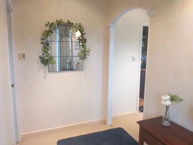 A hallway with a mirror decorated with greenery on the wall a wooden table with a vase of flowers and an arched doorway at The Fairhaven in Tunstall near Catterick North Yorkshire