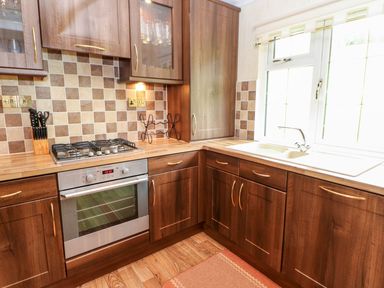 A kitchen with wooden cabinets a gas stove an oven a sink and a window at The Fairhaven in Tunstall near Catterick North Yorkshire