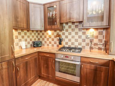 A kitchen with wooden cabinets a built in oven a gas stove a toaster a knife block and tiled backsplash at The Fairhaven in Tunstall near Catterick North Yorkshire