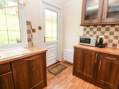 A kitchen with wooden cabinets countertop microwave coffee machine and a door at The Fairhaven in Tunstall near Catterick North Yorkshire