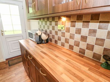 A kitchen countertop with a microwave and coffee machine under wooden cabinets with tiled backsplash at The Fairhaven in Tunstall near Catterick North Yorkshire