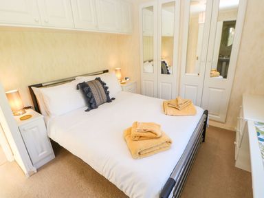 A bedroom with a double bed with white bedding and towels on top bedside tables with lamps and mirrored wardrobes at The Fairhaven in Tunstall near Catterick North Yorkshire