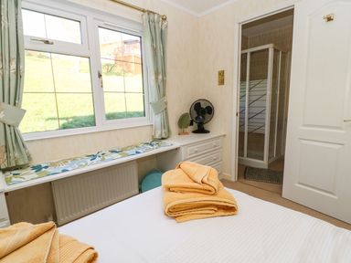 A bedroom with a bed folded towels a window with curtains a chest of drawers with a fan and an open door leading to a shower at The Fairhaven in Tunstall near Catterick North Yorkshire
