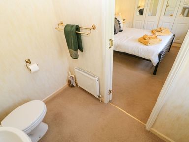 A bathroom with a toilet and green towel next to a bedroom with a bed and folded towels at The Fairhaven in Tunstall near Catterick North Yorkshire